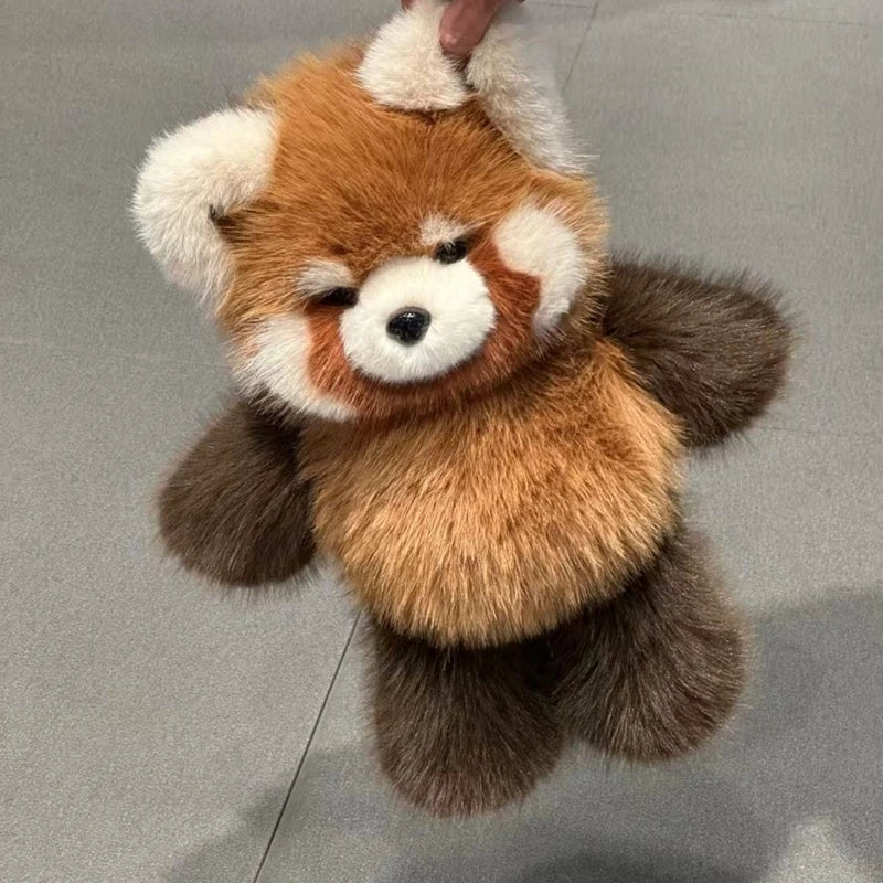 Plush toy red panda held by a hand on a gray background